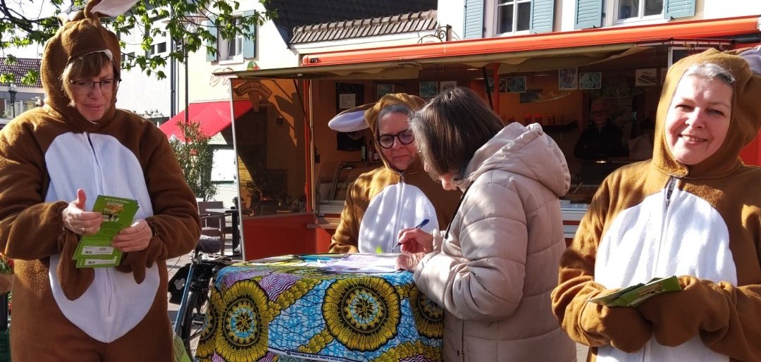 Als Osterhasen verkleidete Frauen sprechen mit einer Frau an einem Stehtisch auf dem Wochenmarkt