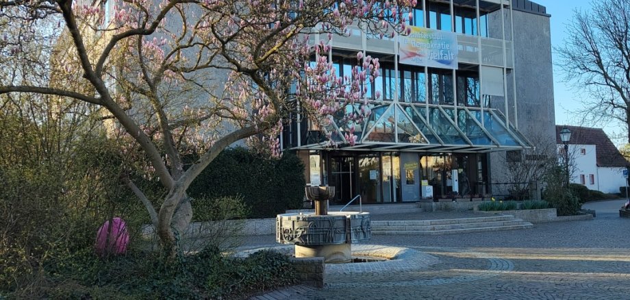 Im Vordergrund ist der blühende Magnolienbaum und der Brunnen mit einem großen Osterei zu sehen, im Hintergrund das Rathaus.
