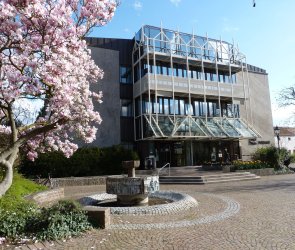 im Vordergrund eine blühende Magnolie und ein Brunnen, im Hintergrund ein Gebäude