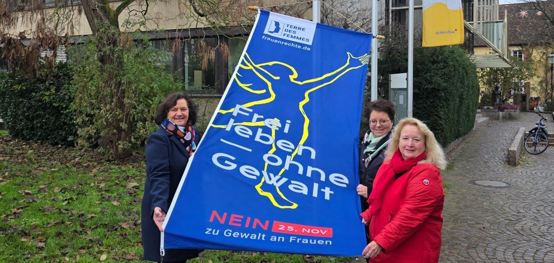 drei Frauen mit Fahne zum Tag gegen Gewalt an Frauen und Kinder
