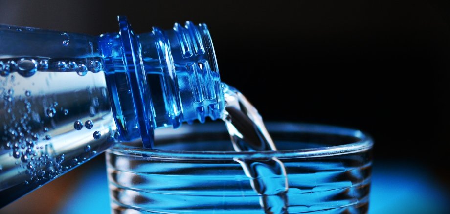 Wasser aus Flasche fließt in ein Glas
