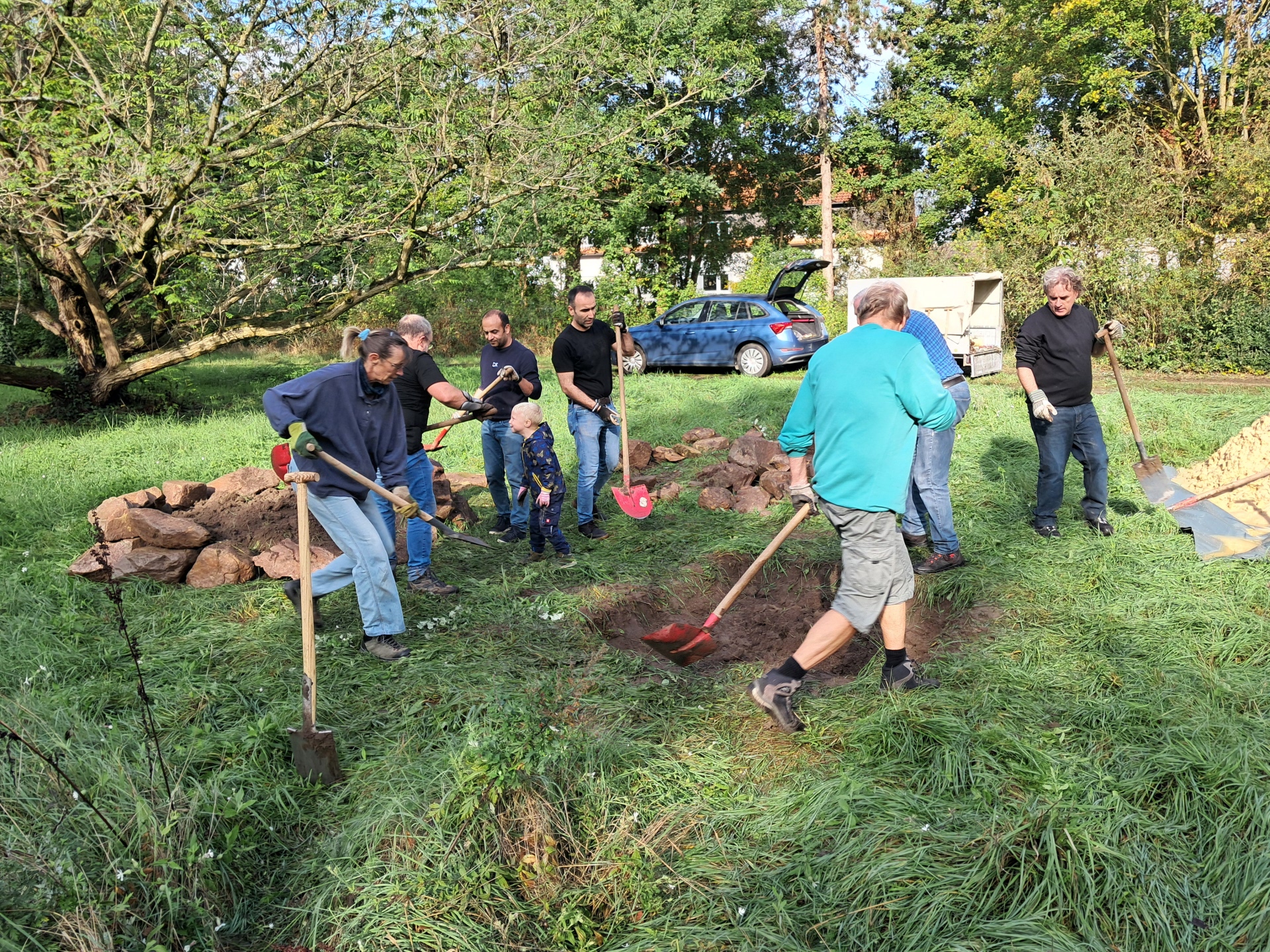 Männer und Frauen mit Schaufeln bearbeiten Bereiche in einer Wiese.