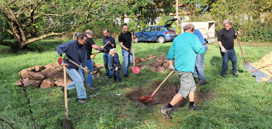 Männer und Frauen mit Schaufeln bearbeiten Bereiche in einer Wiese.