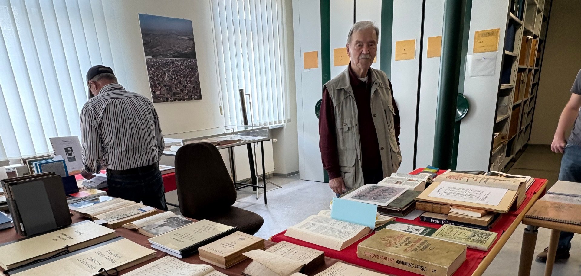 Tische mit Dokumente und Mann im Vordergrund, im Hintergrund ein lesender Mann