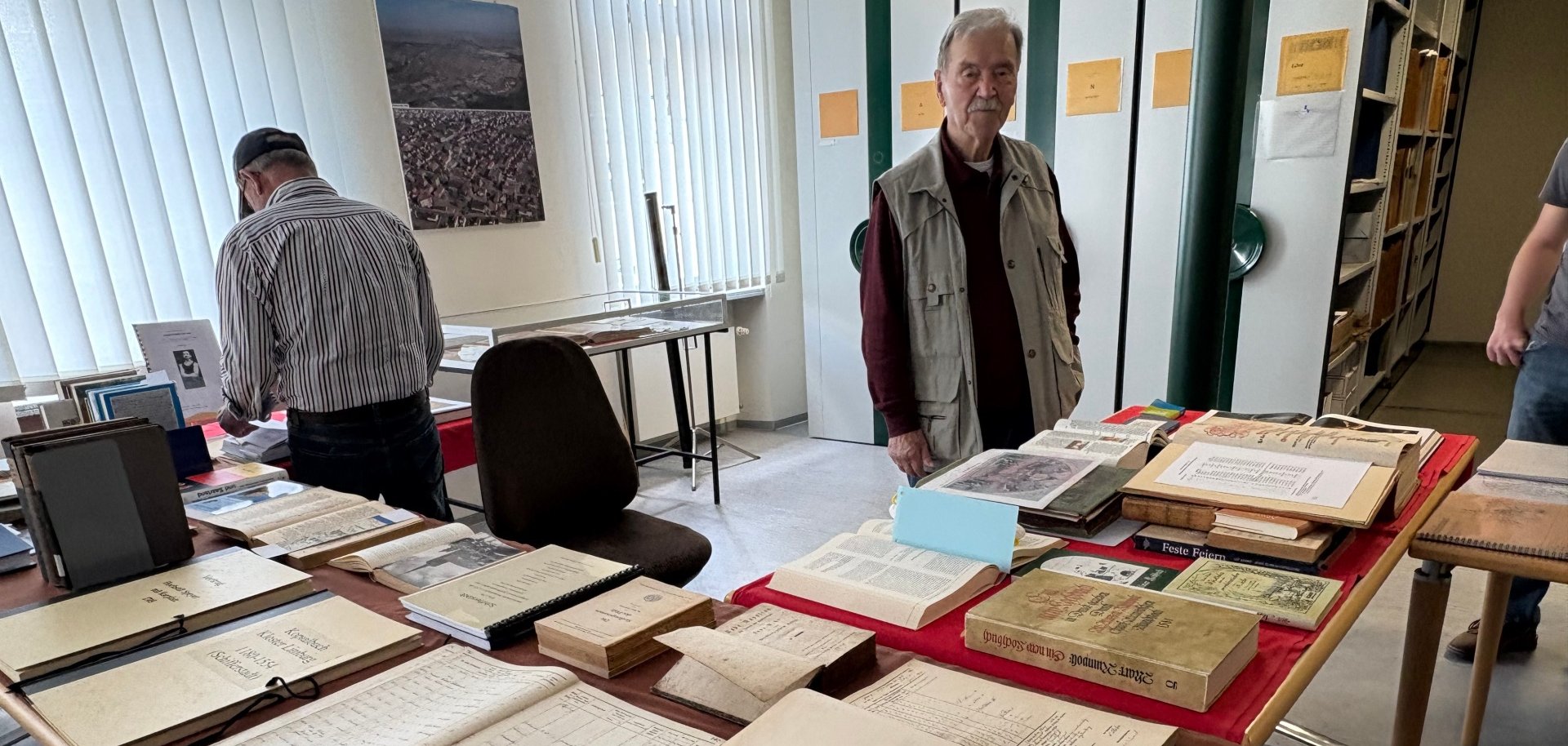 Tische mit Dokumente und Mann im Vordergrund, im Hintergrund ein lesender Mann