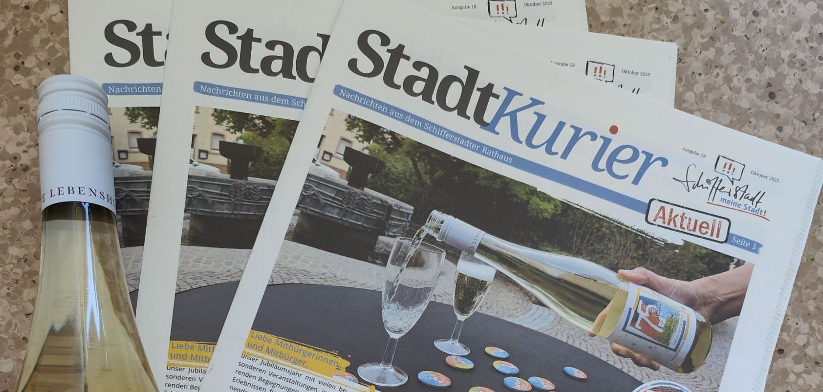 Mehrere Exemplare der Zeitschrift "Stadtkurier" auf einem Tisch mit Sektgläser