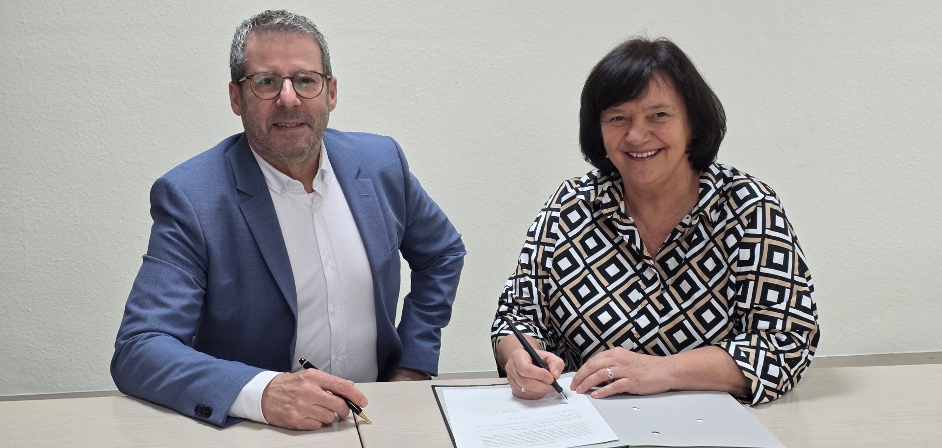 Ein Mann und eine Frau an einem Tisch, die Frau hat einen Stift in der Hand, vor ihr liegt ein Schriftstück