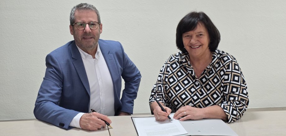 Ein Mann und eine Frau an einem Tisch, die Frau hat einen Stift in der Hand, vor ihr liegt ein Schriftstück