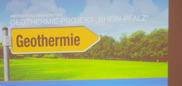 zwei Männer im Vordergrund, im Hintergrund ein Bild mit Wegweiser "Geothermie"