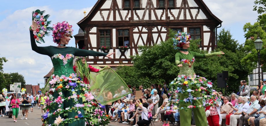 Drei als Blumenfrauen geschmückte Stelzenläuferinnen