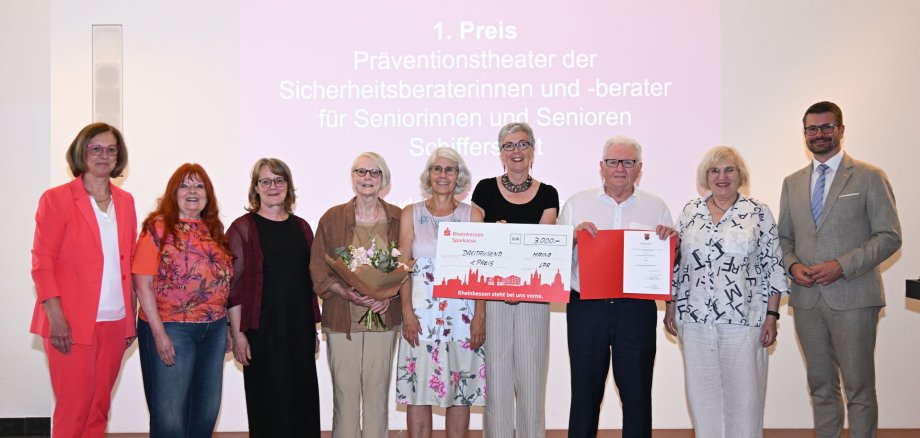 Sieben Frauen und zwei Herren stehen in einem Halbkreis und zeigen einen Scheck und eine Urkunde